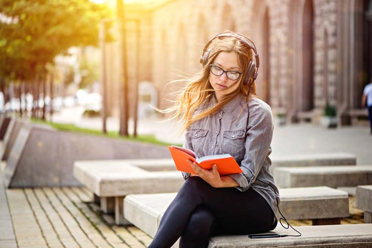 Female student reading a book while wearing headphones