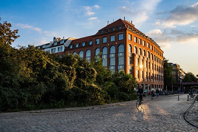 Students cycling in front of large building as sun sets