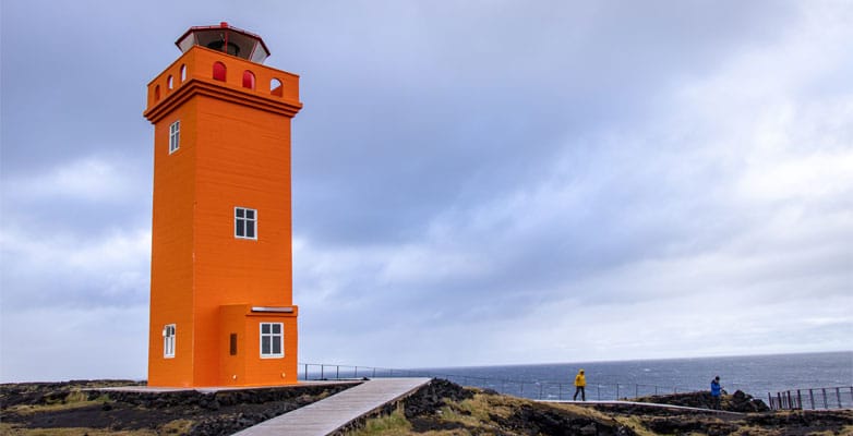 An orange lighthouse pictured in front of a body of water
