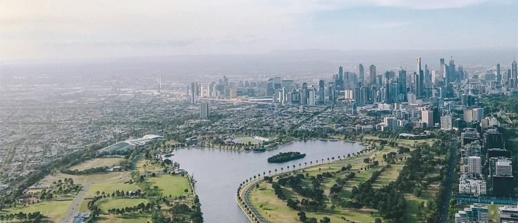 the city skyline of Melbourne with green space and a lake in the foreground