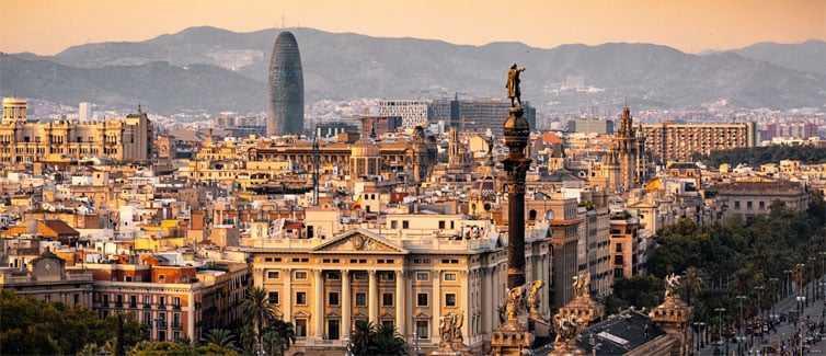 Panoramic picture of the city of Barcelona with buildings in the foreground and mountains and the sun in the background