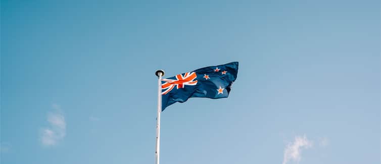 Image of the New Zealand flag flying on a flagpole with a blue sky background