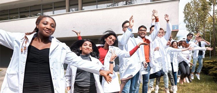 A group of students all wearing medical style white laboratory coats smiling at the camera