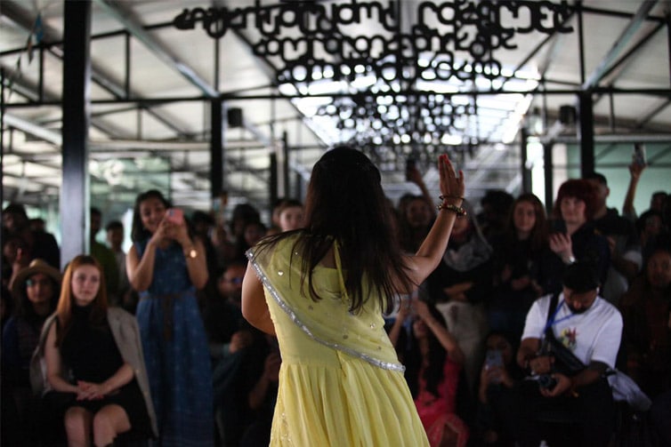 Image of a group of people watching a person in a yellow dress performing a dance move