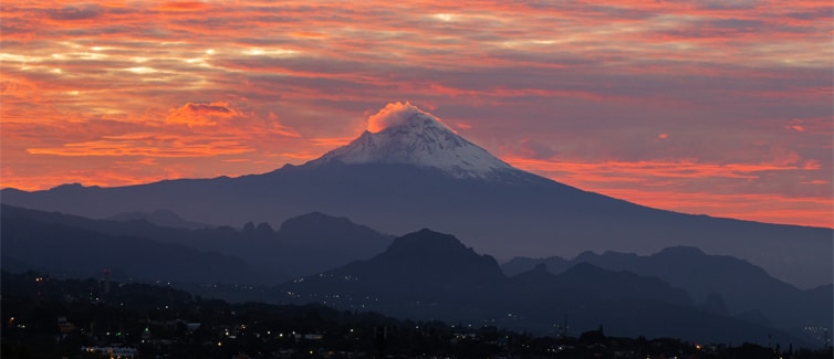 Tall snow-topped mountain with a orangey pink sky in the background