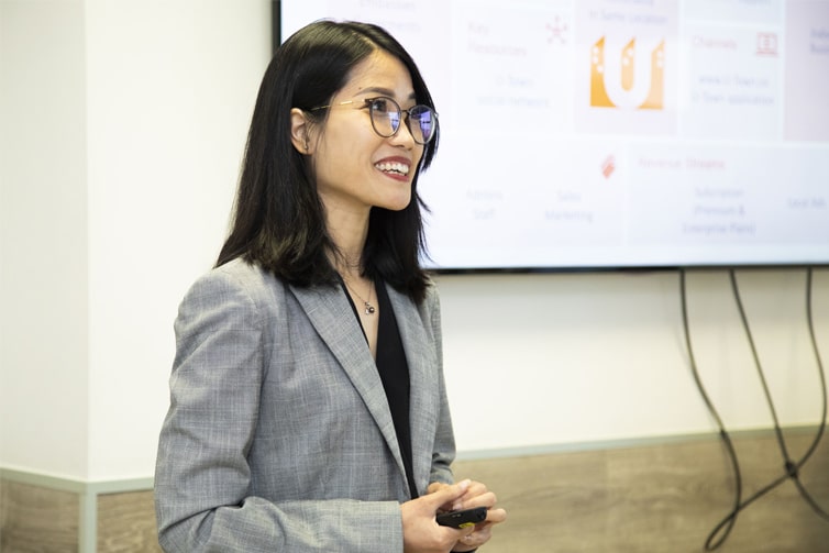 Image of a smartly dressed student standing next to a presentation board, smiling away from the camera