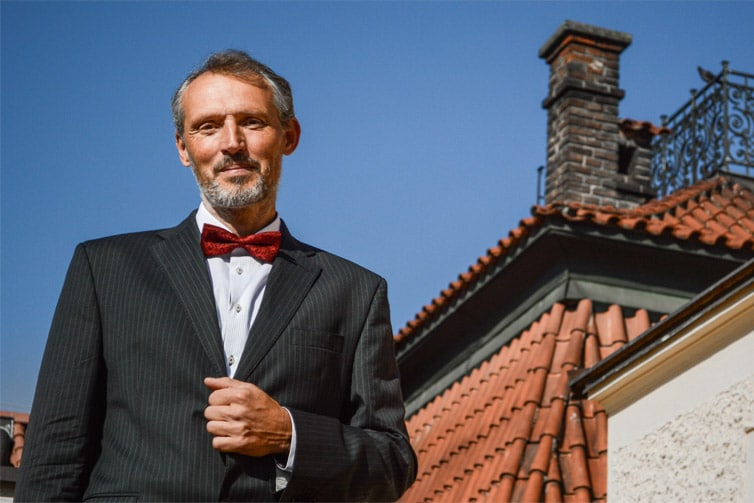 Image of a man standing in front of a building with a red bow tie and suit on