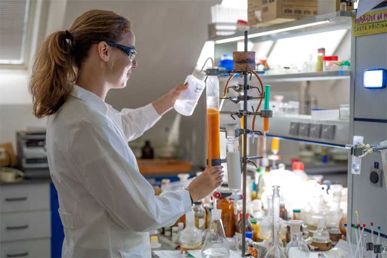Image of a student using scientific equipment wearing a white lab coat and lab goggles