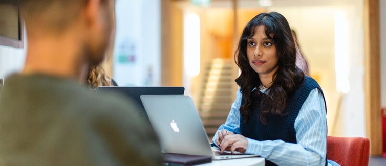 Image of two students, one facing the camera and one with their back to the camera.