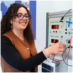 Image of a student wearing glasses looking at a machine with wires coming out of it