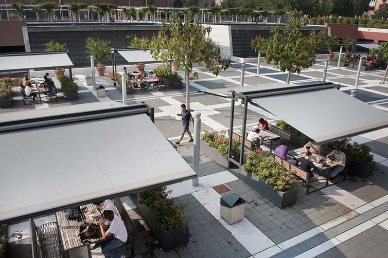 Students sitting at outdoor tables under grey awnings
