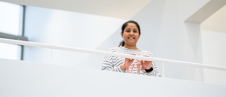Image of a student standing behind a white banister smiling at the camera