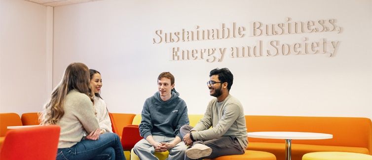 Image of four students sat on a bright orange sofa smiling at each other